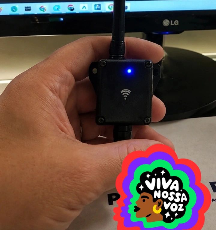 O sensor: caixa preta com antena de wifi e LED azul aceso, na mão